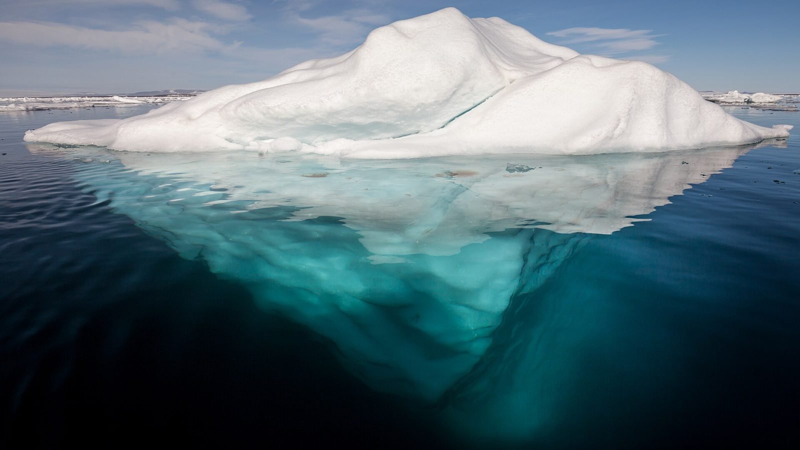 An Arctic iceberg: a small white peak above the waterline and a much larger mass visible below the surface